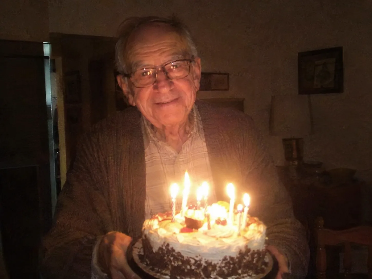 Original photo: an older man holding a birthday cake in a dim room